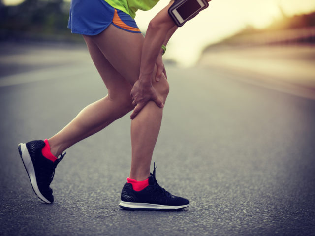 Sportswoman suffering from knee pain while running on city road