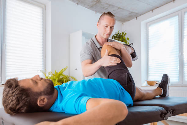 Physical therapist giving leg massage to young man. Patient lying down on massage table.