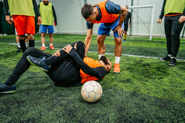 Amateur soccer player got injured in the game. He is lying on field in pain.