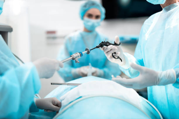 Close up of male and female hands holding laparoscopic grasper with trocar. Female medical worker holding oxygen mask on patient face on blurred background for minimally invasive surgery