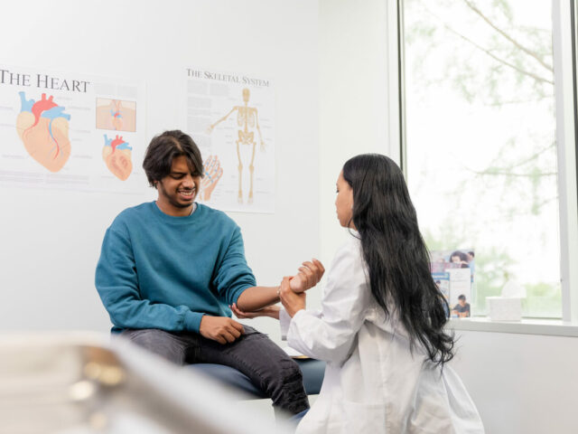 emale orthopedist moves his arm, man reacts in pain in orthopedic clinic