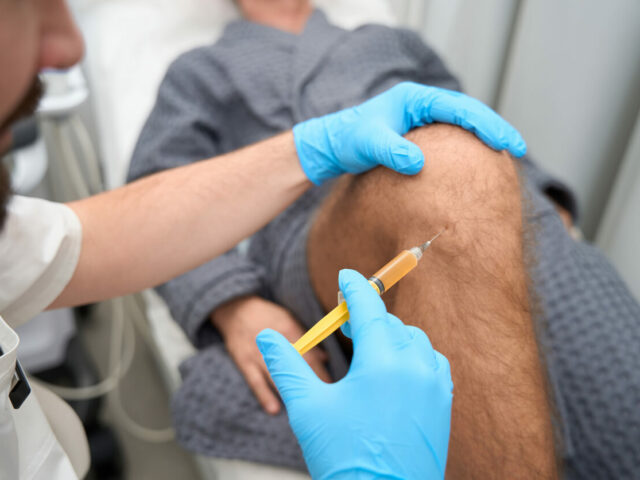 Experienced doctor taking a biopsy sample from a male knee for stem cell therapy.
