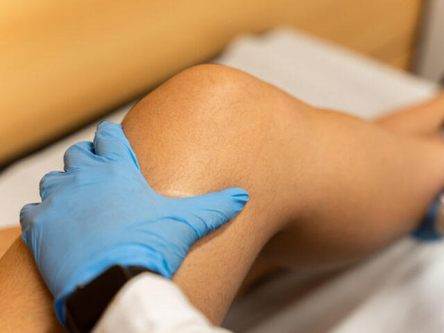 A sports medicine physician examines the knee joint of a woman experiencing pain from an ACL tear.