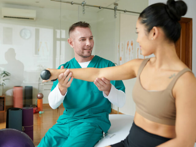 A male orthopedic expert assisting a female patient with the process of rebuilding arm strength at an orthopedic clinic.
