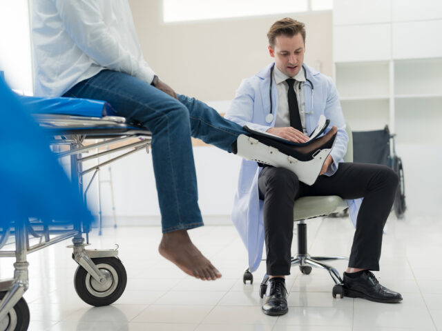 A male orthopedic expert doctor puts a splint on a patient with a leg injury at an orthopedic clinic.