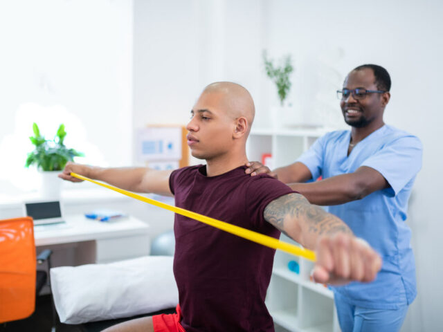 A sportsman with his arms stretched out, holding a ribbon, is visiting a sports medicine doctor.
