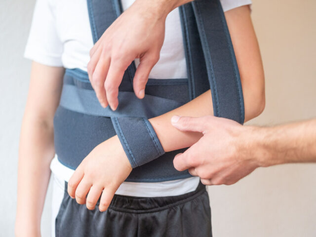 A teenage boy with a fractured arm in an orthopedic sling at an orthopedic clinic.