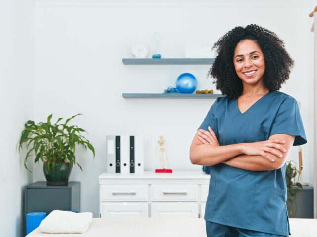 Confident Female Orthopedic Specialist in Blue Scrubs Standing with Arms Crossed in Orthopedic Clinic.
