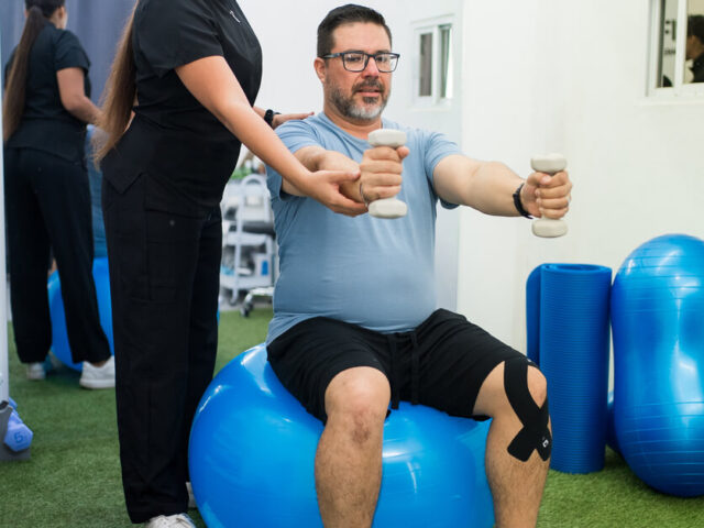 A female sports medicine doctor is assisting a man with rehabilitation exercise on stability ball.